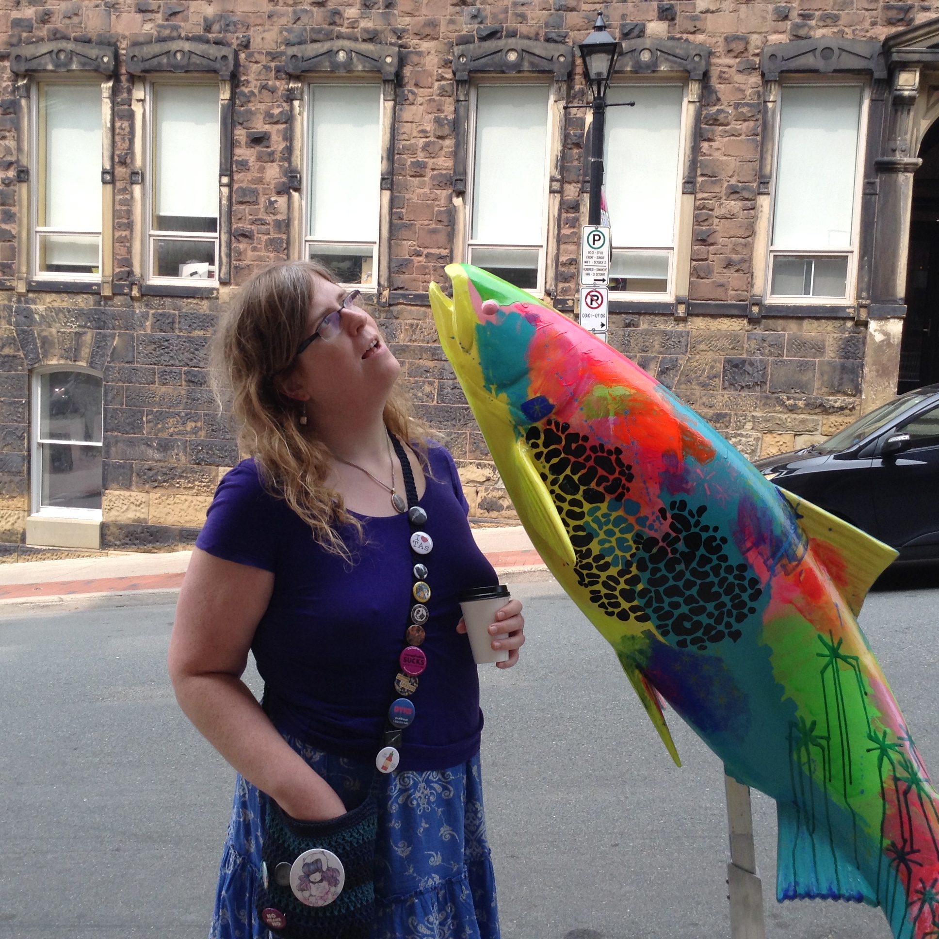 A photo of me, posing with a rainbow painted fish sculpture.